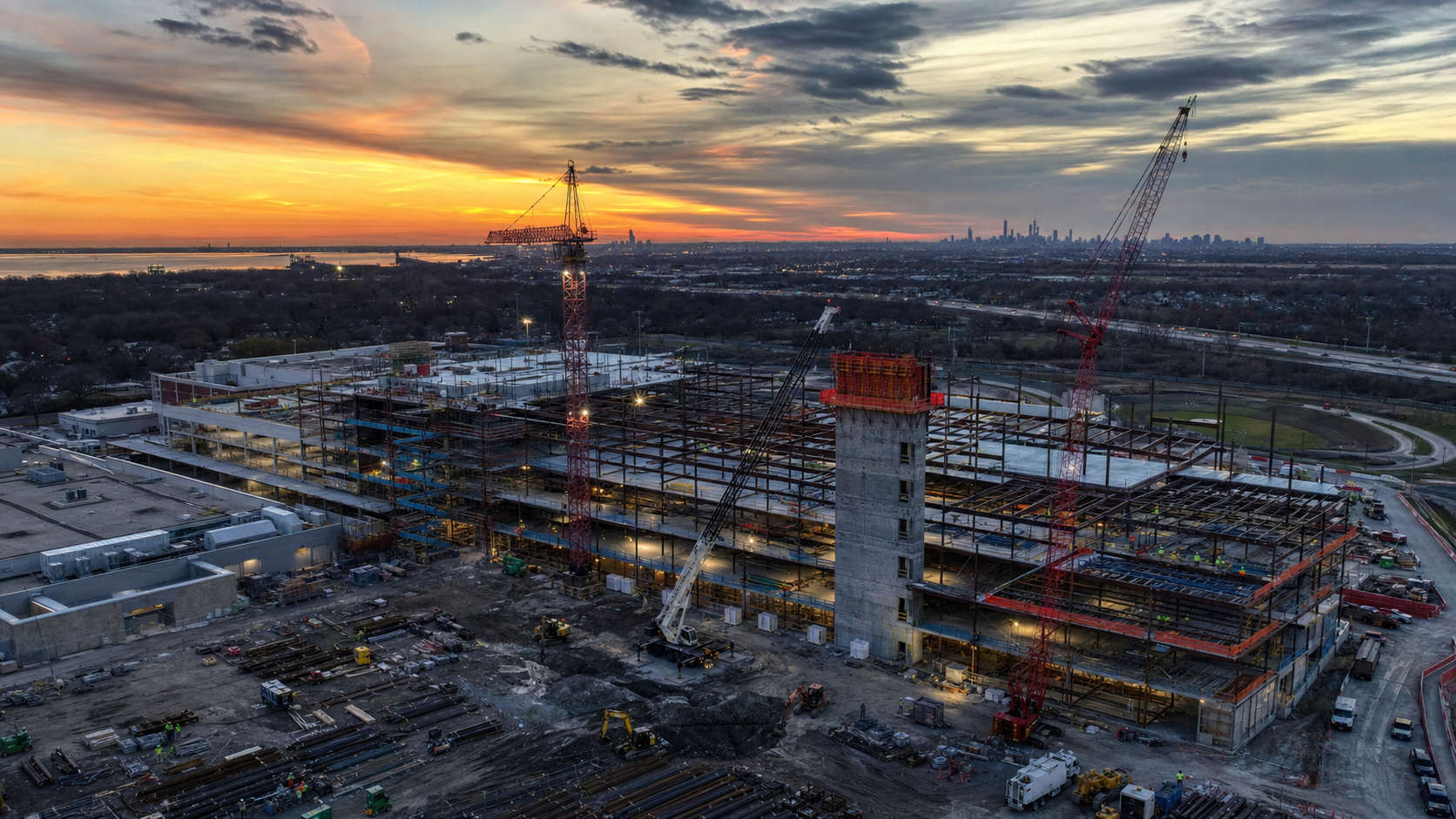 Wide aerial photograph of a commercial construction site at dusk with tower cranes