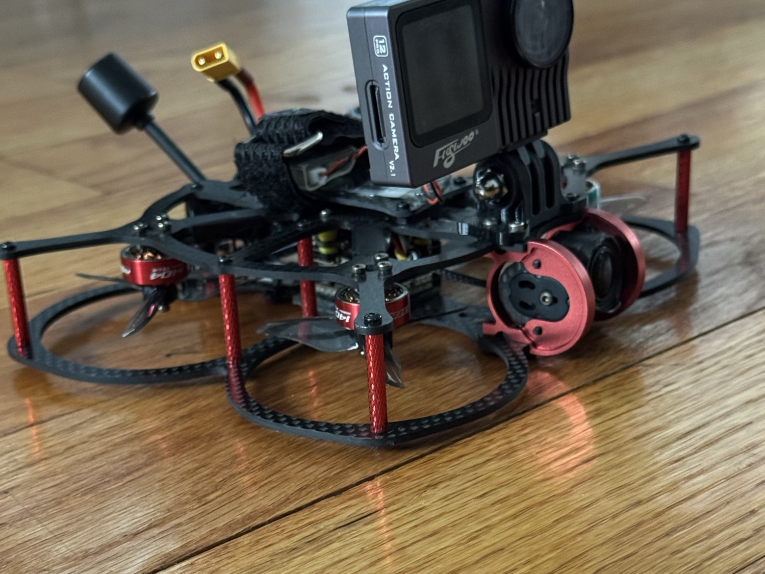 Val's Aerial Solutions red and black FPV cinewhoop drone with action camera, resting on a wood floor