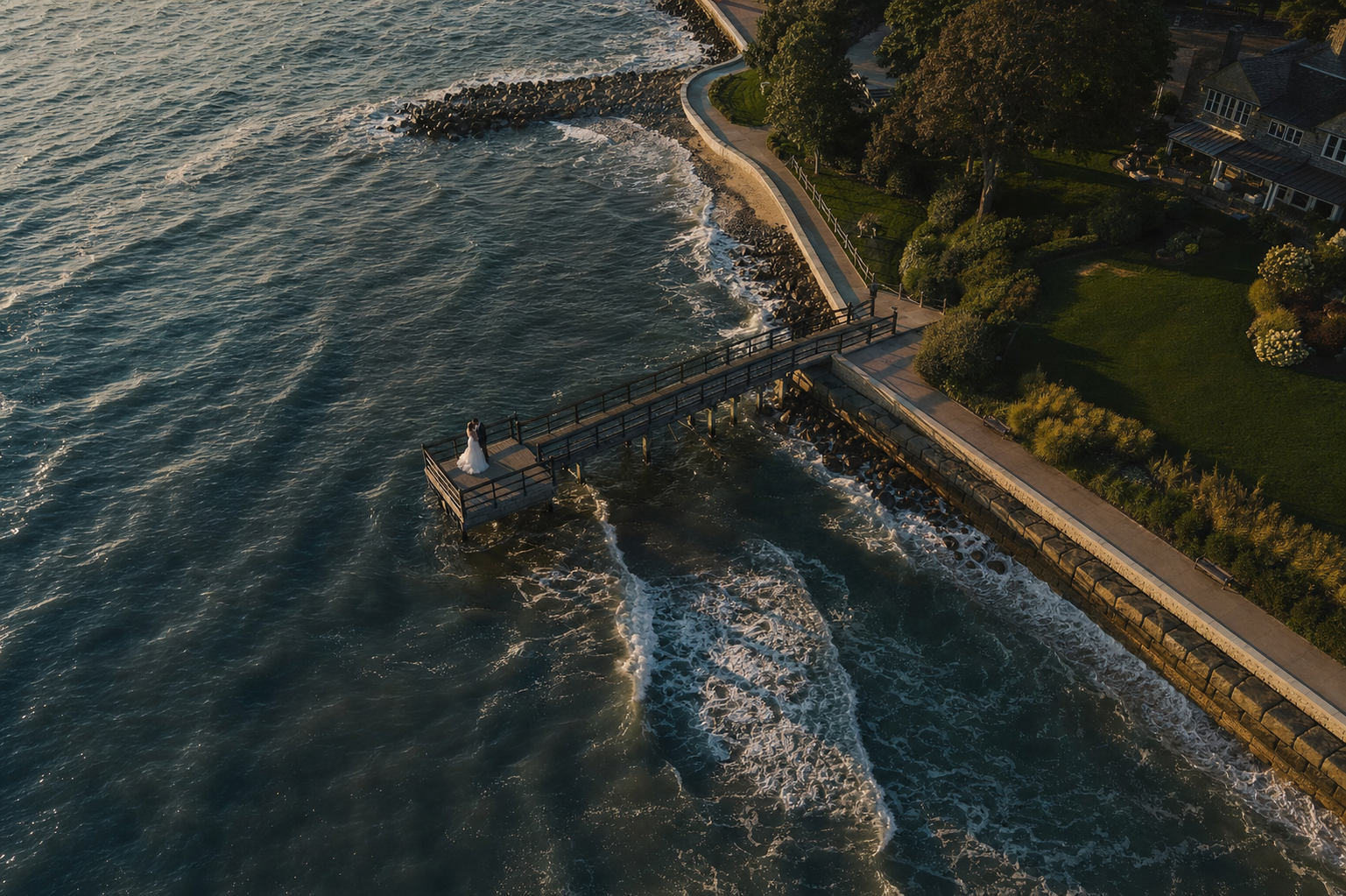 Aerial shot of newlyweds on a shoreline pier at golden hour