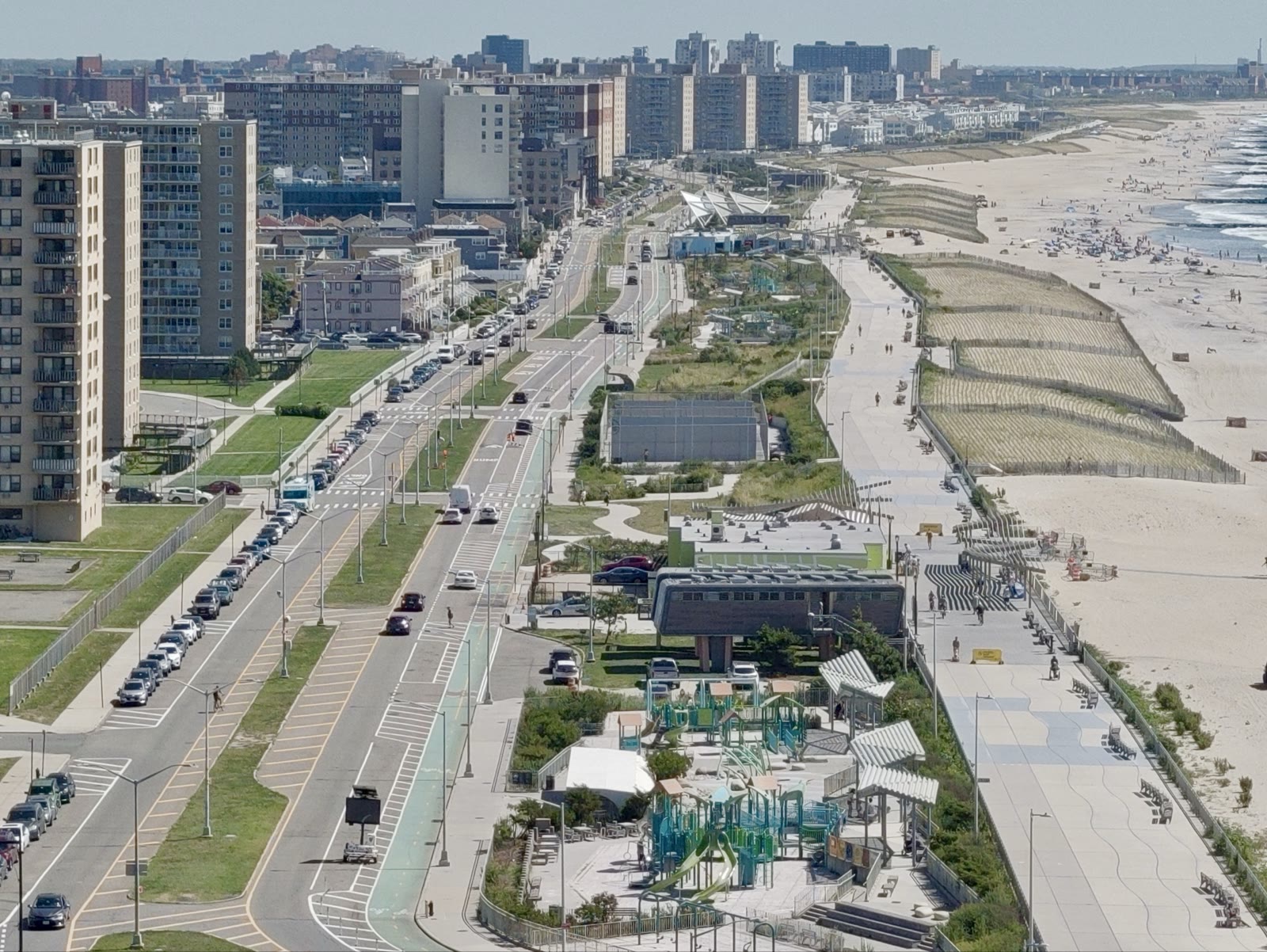 Aerial drone photograph of a boardwalk and beach with the New York City skyline visible in the distance
