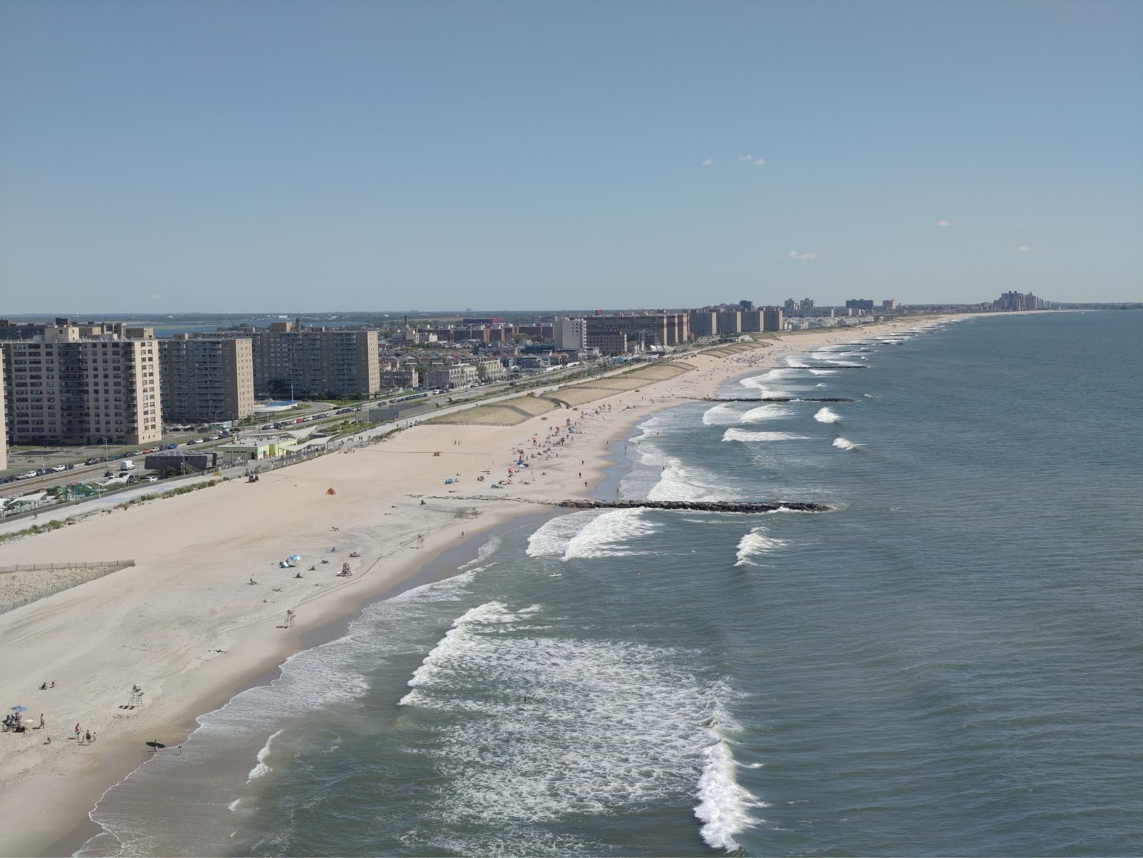 Aerial drone photograph of Atlantic Ocean waves rolling into a wide sandy beach with a coastal skyline in the distance